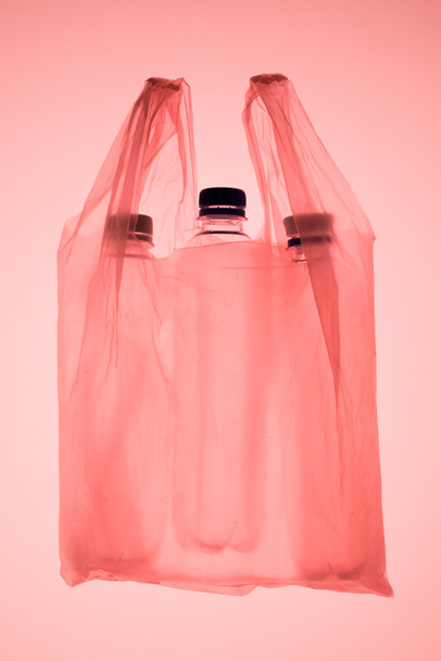 transparente Plastiktüte mit Plastikflaschen unter pastellrosa getöntem Licht - Foto, Bild