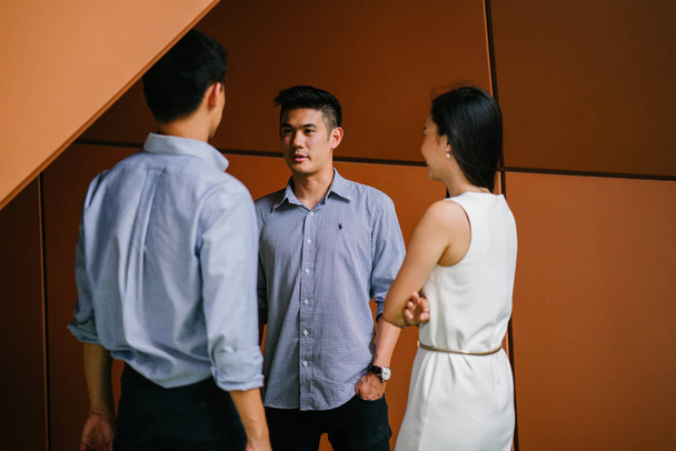 team of three business professionals (lawyers, bankers or accountants) have a conversation / discussion in their office in the day. Two Chinese Asian men and a woman stand together and are talking. - Φωτογραφία, εικόνα