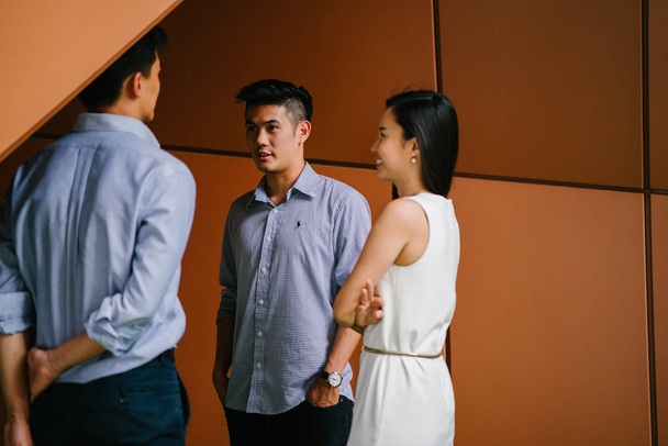 team of three business professionals (lawyers, bankers or accountants) have a conversation / discussion in their office in the day. Two Chinese Asian men and a woman stand together and are talking. - Photo, image