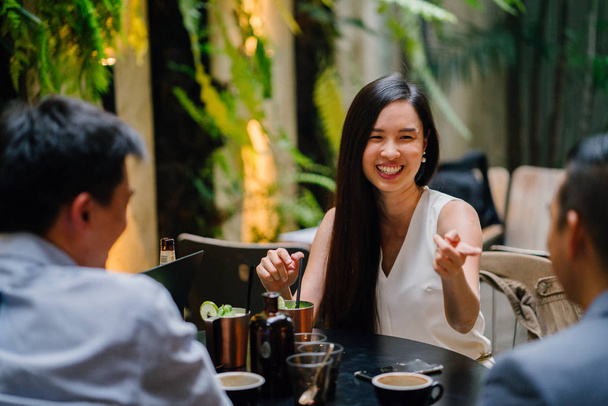 young Chinese woman professional (lawyer, banker, lawyer, etc) smiles and laughs as she has a discussion with coworkers in a trendy coworking space or office over drinks. She is young and attractive - Foto, Bild