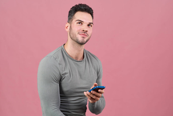 portrait of a young athletic man mysteriously smiling, looking up and holding a smartphone. - Foto, afbeelding