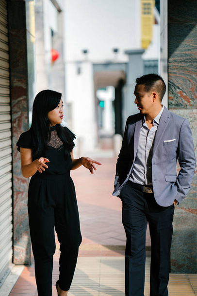 portrét dvou profesionálních obchodních lidí chodí a mluví. Jsou hluboko v rozhovoru, jak chodí na ulici ve městě, v Asii. Muž a žena jsou profesionálně oblečený. - Fotografie, Obrázek