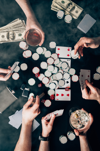 Smoke over people with alcohol in glasses playing poker by casino table with money and chips - Foto, afbeelding