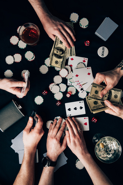 People playing poker by casino table with money and chips - Foto, afbeelding