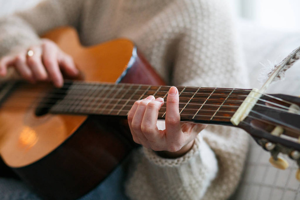 Play the guitar by hand Artist or musician.Young woman hands in knitted sweater. Home music party - Foto, imagen