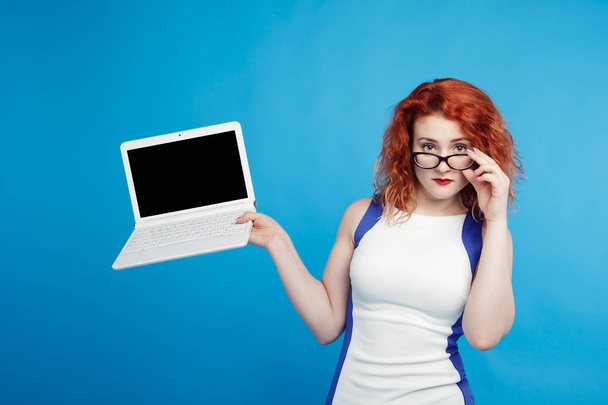 beautiful red-haired girl holding a laptop isolate on a blue background. place for text - Foto, imagen