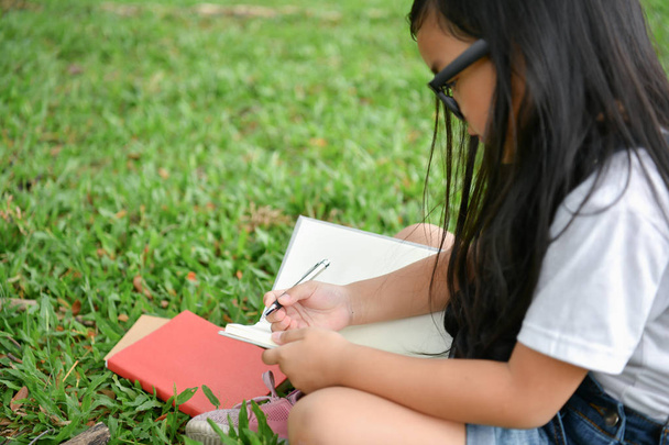 Koulutuksen käsitteet. Tyttö on lukemassa kirjaa puutarhassa. Ole
 - Valokuva, kuva