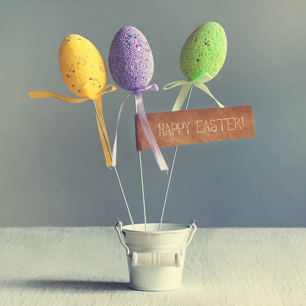 Színes húsvéti tojást a kis fehér vödör botokkal. A felirat a Boldog húsvéti. Másolja a hely. - Fotó, kép