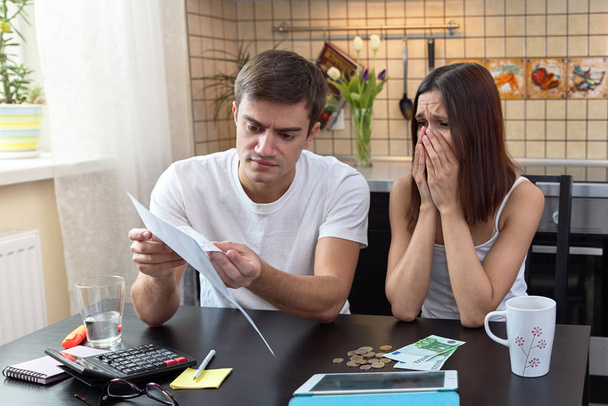 young couple sits at a table in the kitchen and is engaged in the calculation of the home budget, financial assets.  - Foto, Bild