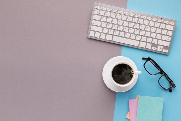 Γραφείο με φλιτζάνι καφέ και το πληκτρολόγιο σε δυο χρώματα φόντου - Φωτογραφία, εικόνα