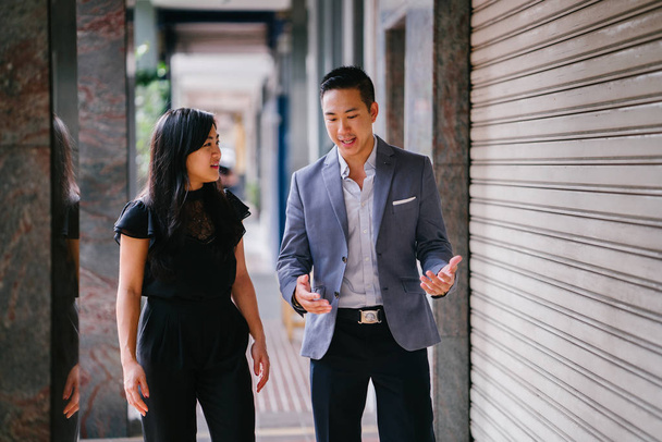 portrait of two professional business people walking and talking. They are deep in conversation as they walk on a street in a city in Asia. The man and woman are both professionally dressed. - Photo, image