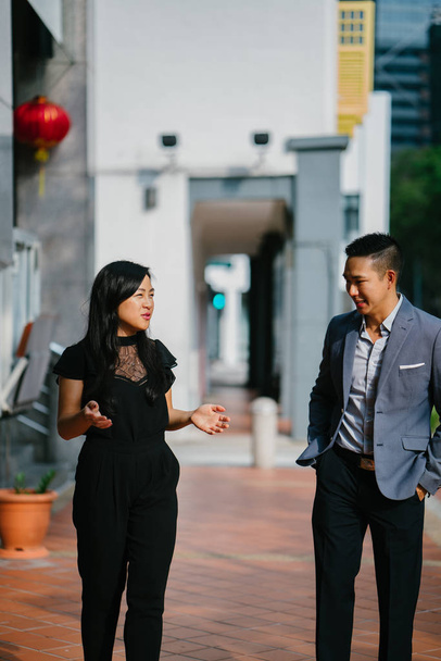 portrait of two professional business people walking and talking. They are deep in conversation as they walk on a street in a city in Asia. The man and woman are both professionally dressed. - Foto, Imagen