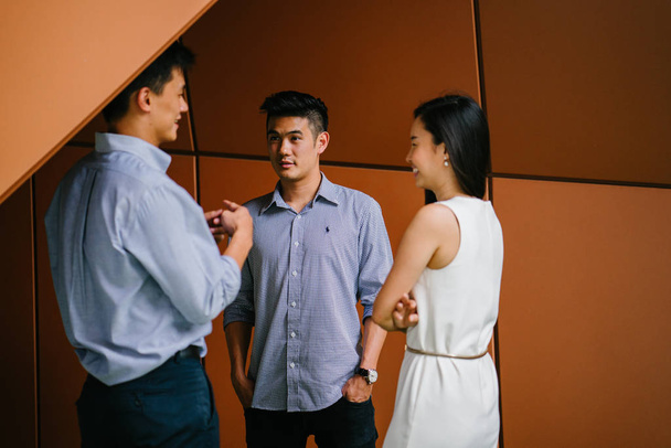 team of three business professionals (lawyers, bankers or accountants) have a conversation / discussion in their office in the day. Two Chinese Asian men and a woman stand together and are talking. - Fotoğraf, Görsel