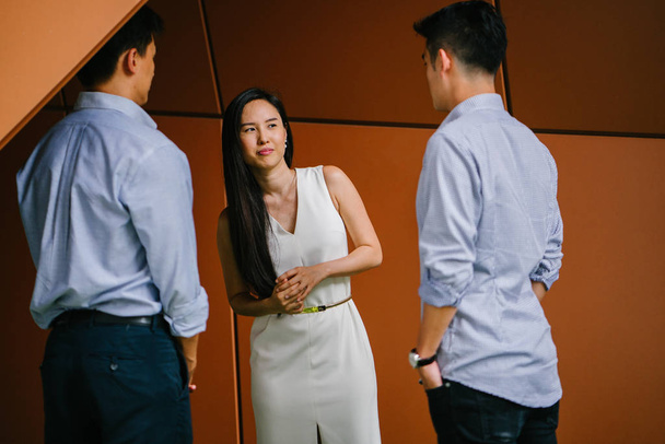 team of three business professionals (lawyers, bankers or accountants) have a conversation / discussion in their office in the day. Two Chinese Asian men and a woman stand together and are talking. - Foto, afbeelding