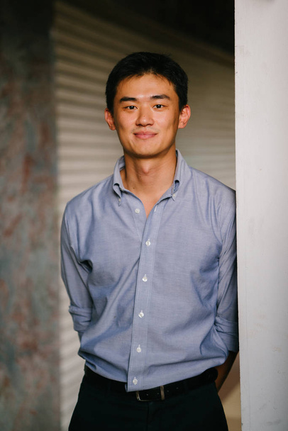 Portrait of a young, handsome, tall and professional Chinese man standing against a pillar in the day. He is a lawyer, banker or some other professional and is smiling at the camera. - Zdjęcie, obraz