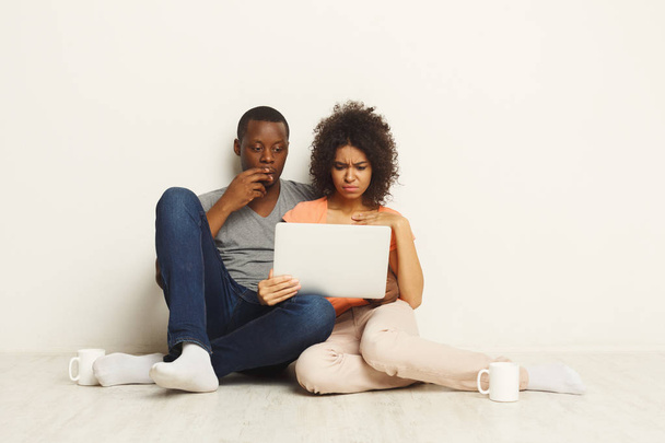 Shocked couple using laptop, sitting on floor - Foto, imagen
