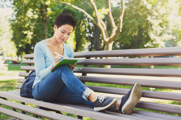 Shorthaired female student writing outdoors - 写真・画像