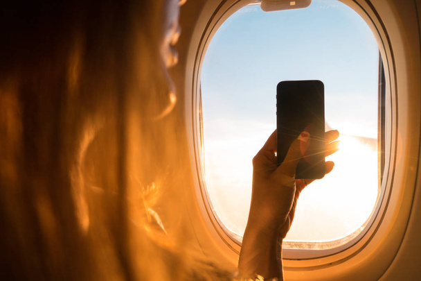 Фотография на самолете, Путешествия аксессуары для быстрого момента, Рука держит смартфон и фотографировать, Камера для путешествий аксессуары, Фотография в воздухе
. - Фото, изображение