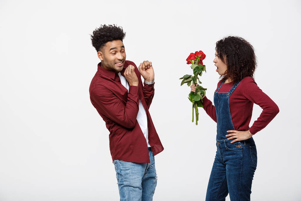 Portrait of a disappointed young woman holding red rose with while standing and angry on her boyfriend isolated over white background - Photo, Image