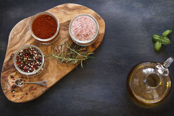 close-up photo of colored dried spices in bowls on wooden board on black concreted table background with olive oil in jar  - Foto, afbeelding