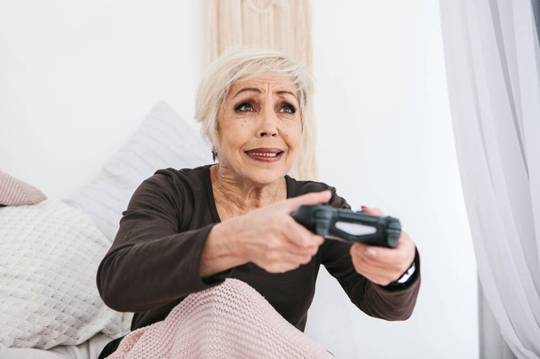 An elderly woman is playing a video game. Elderly person and modern technology. - Photo, image