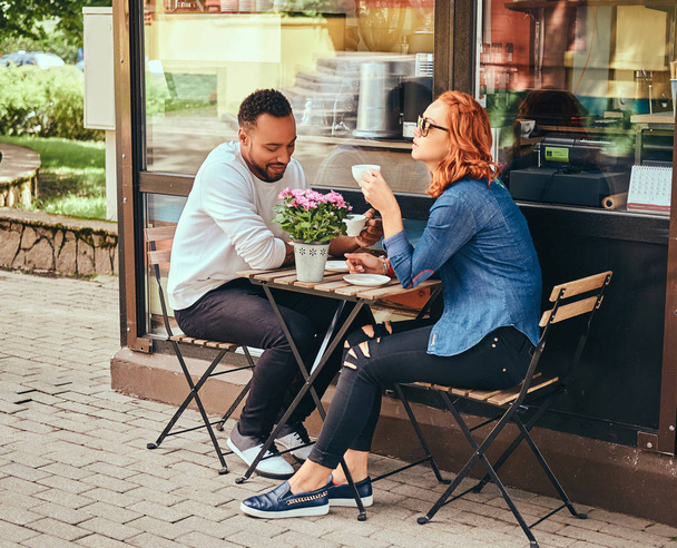 Ζευγάρι γνωριμίες πίνοντας καφέ, κάθονται κοντά στο κατάστημα καφέ. Σε εξωτερικούς χώρους σε μια ημερομηνία. - Φωτογραφία, εικόνα