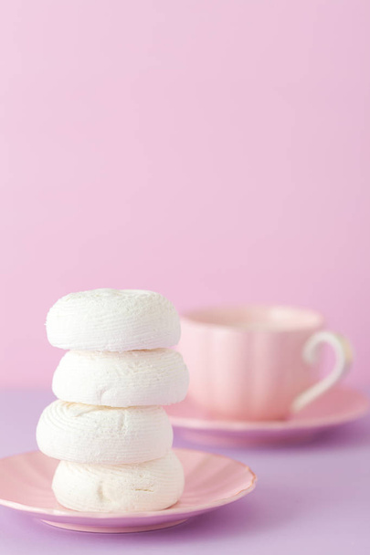 Banner vertical de color violeta pastel y rosa con espacio para copiar - zephyr blanco en el plato y taza de café con leche
. - Foto, Imagen