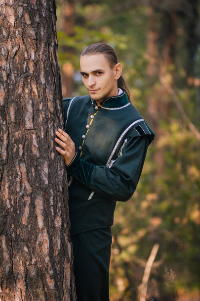 Un tipo sexy en el bosque. En ropa hermosa y vieja de color verde. Un medieval. Fantasía
.  - Foto, imagen