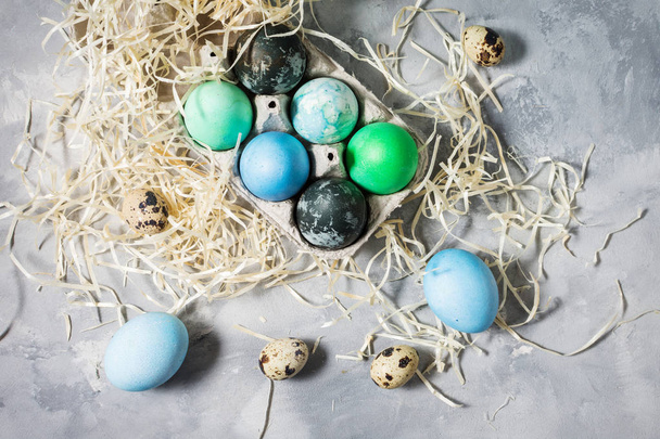 окрашенные яйца в лоток, перепелиные и куриные яйца, краска и кисть на бетонной поверхности, пасхальные украшения
 - Фото, изображение