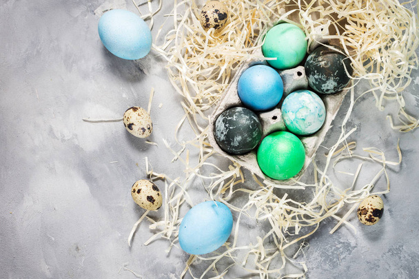 bemalte Eier in Tablett, Wachtel- und Hühnereier, Farbe und Pinsel auf Betonoberfläche, Osterdekorationen - Foto, Bild