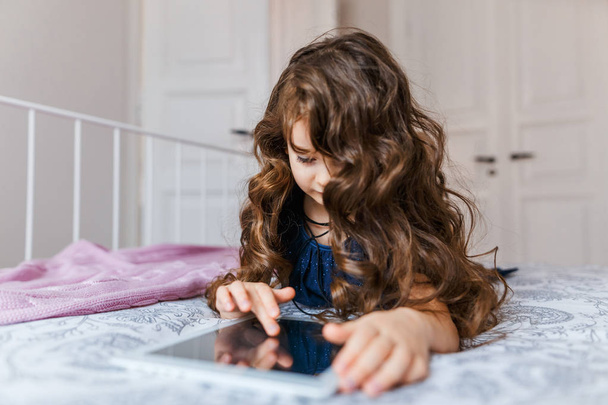 Cute little girl with curly hair using digital tablet  - Fotó, kép
