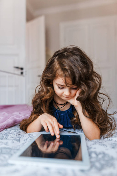 Cute little girl with curly hair using digital tablet  - Фото, изображение