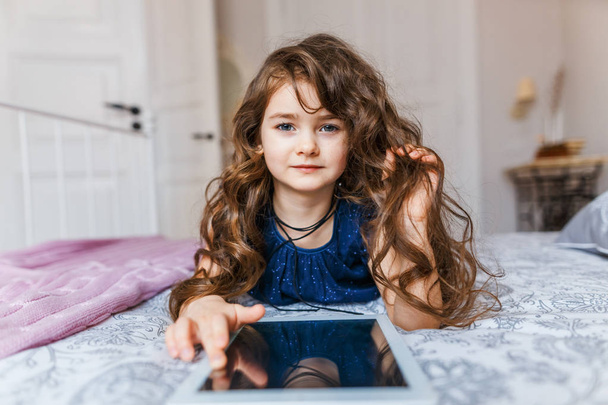 Cute little girl with curly hair using digital tablet  - Fotó, kép
