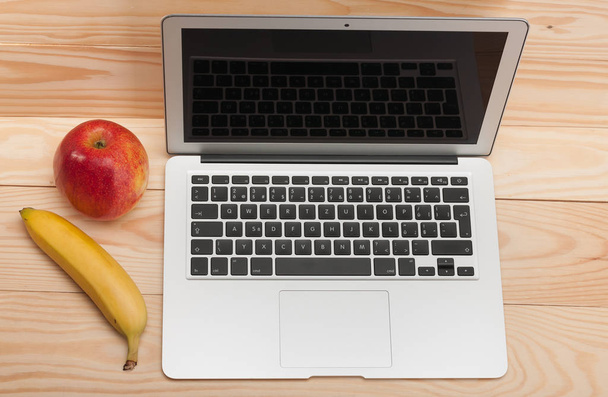Ανοίξτε το φορητό υπολογιστή με μπανάνα και μήλο σε ξύλινο φόντο - Φωτογραφία, εικόνα