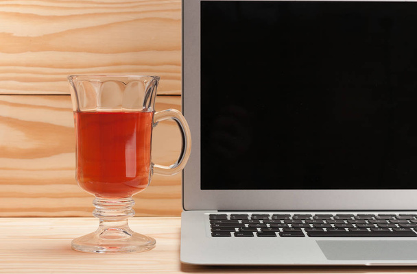 Open laptop with cup of tea on wooden background - Photo, Image