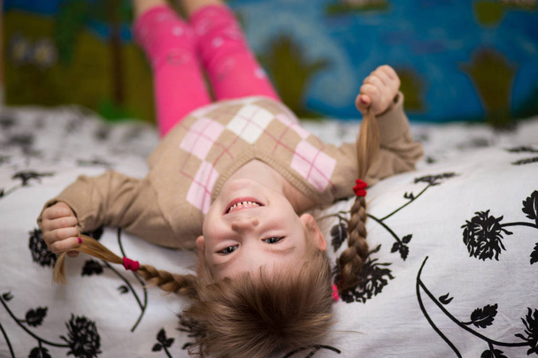 Funny girl lying in bed. Little girl has fun in bed. Concept of kids sleep, care or childhood - Foto, Imagen