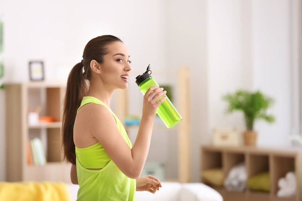 Beautiful young woman drinking water after doing fitness exercises at home - Фото, зображення