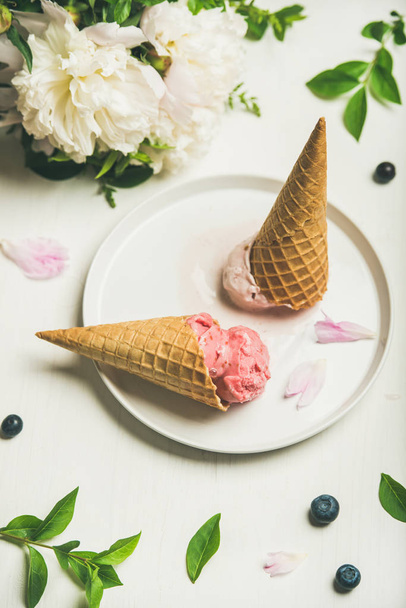 Pink strawberry and coconut ice cream scoops, sweet cones and peony flowers bouquet on plate over white background - Φωτογραφία, εικόνα
