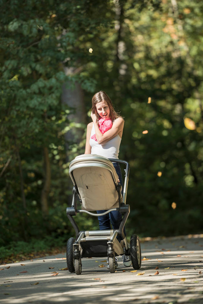 Smiling mother pushing a baby carriage along a rural road - Foto, immagini