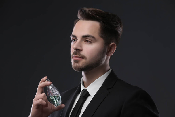 Handsome man in suit using perfume on dark background - Fotoğraf, Görsel