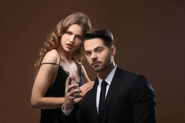 Passionate woman and handsome man using perfume on color background - Foto, Imagen