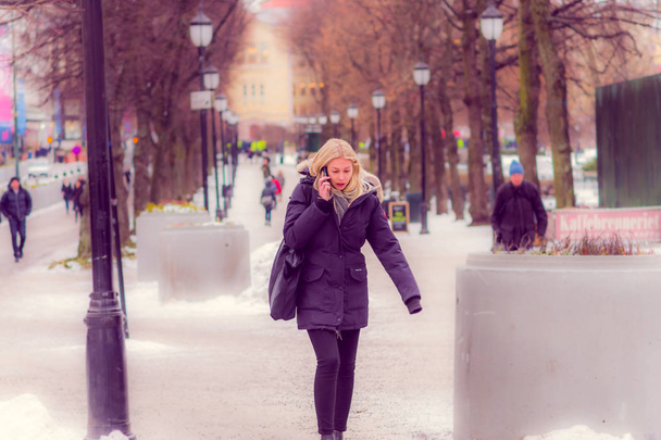 OSLO, NORWAY - MARCH, 26, 2018: Outdoor view of beautiful blonde woman using her cellphone and walking in a public park in Oslan - Foto, immagini