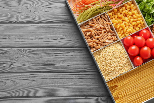 Коробки с различными сырыми макаронами и продуктами на деревянном фоне
 - Фото, изображение