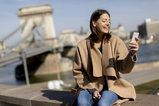 junge Frau benutzt Handy mit Kettenbrücke im Hintergrund in Budapest, Ungarn - Foto, Bild