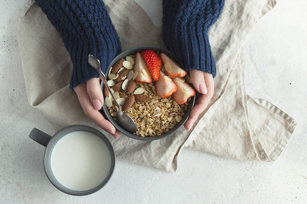 Healthy breakfast. Grey ceramic bowl with granola, strawberry and nuts in woman's hands. Diet and vegetarian food concept - 写真・画像