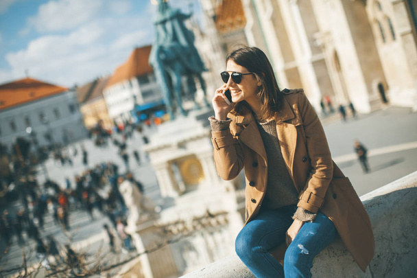 Katso trendikäs nuori nainen istuu ulkona ja käyttää matkapuhelinta
 - Valokuva, kuva