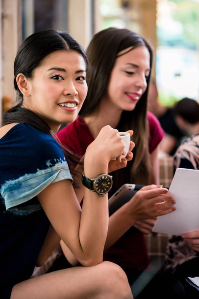 Young woman showing paperwork to her friends while sitting together in a coffee shop - Photo, Image