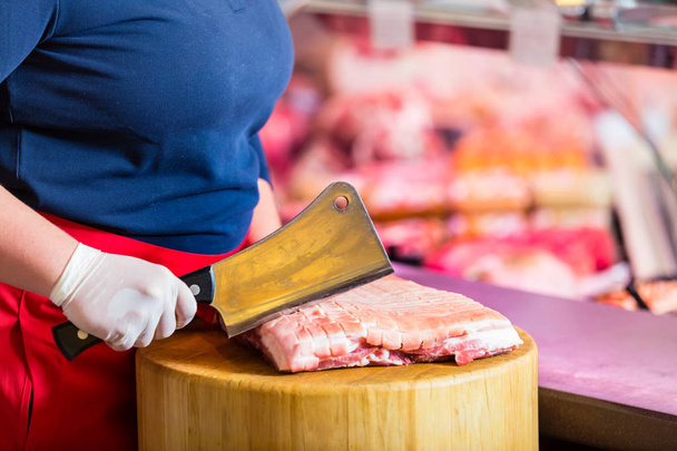 Mulher açougueiro cortando carne em um bloco com faca grande
 - Foto, Imagem