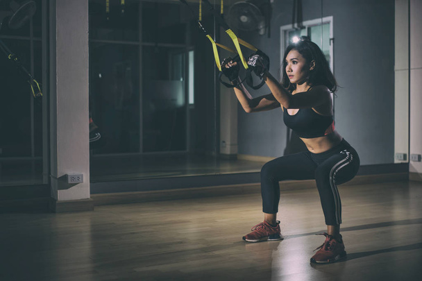 Ισχυρή γυναίκα κάνει trx άσκηση με ιμάντες σε γυμναστήριο. - Φωτογραφία, εικόνα