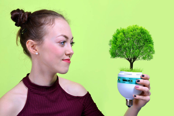 Girl holding eco light bulb with tree in hand. Green energy concept - Φωτογραφία, εικόνα